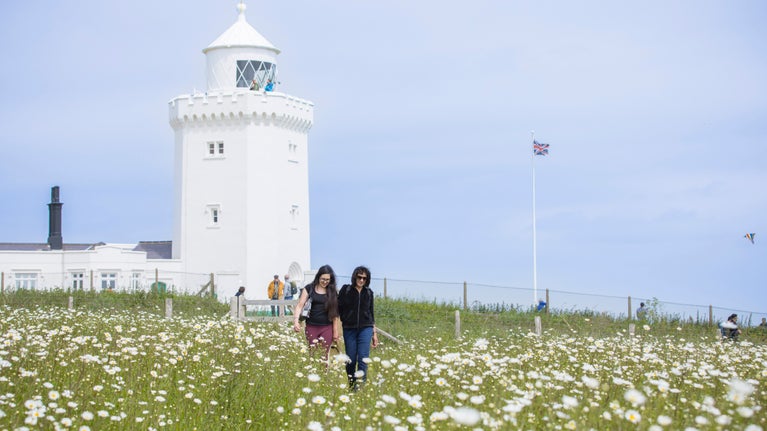 People walk through a coastal meadow at South Foreland Lighthouse on The White Cliffs of Dover, Kent
